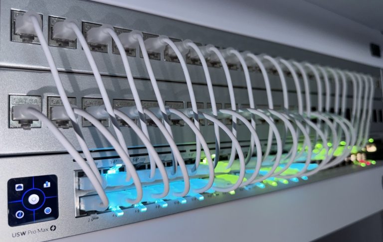 Baie réseau professionnelle avec switch Ubiquiti, cordons RJ45 blancs et voyants d'activité
